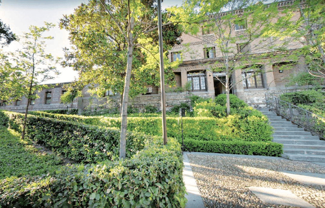 Casa de piedra rodeada de exuberante vegetación y árboles, con un camino de grava y una escalera que conduce a la entrada.